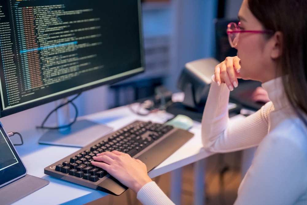 Entwicklerin sitzt vor einem Monitor mit geöffnetem Code-Editor und analysiert Website-Code bei gedämpftem Licht